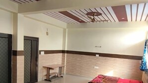 A hotel room with two beds, a ceiling fan, a small table, and a wall-mounted light. - Sudama Krishna Residency (Mathura)