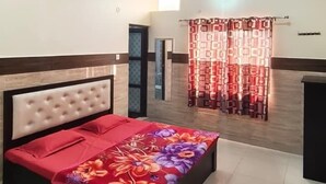 A bedroom with a bed, a ceiling fan, and a window with curtains. - Sudama Krishna Residency (Mathura)