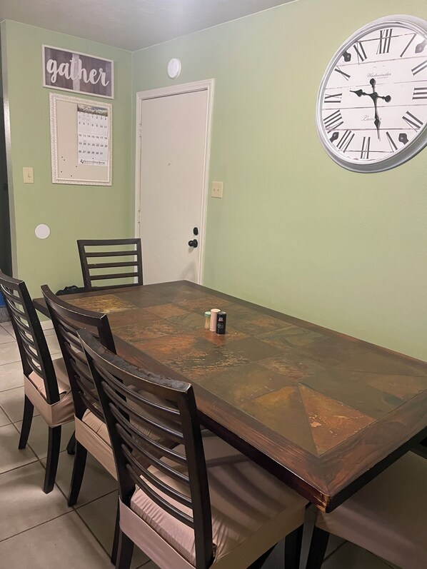 A dining area with a wooden table, four chairs, a wall clock, and a door. - King Suite 3Bed/2Bath (Bryan)