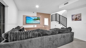 Un salon moderne avec un grand canapé d’angle, un téléviseur à écran plat, un meuble en bois et un escalier.