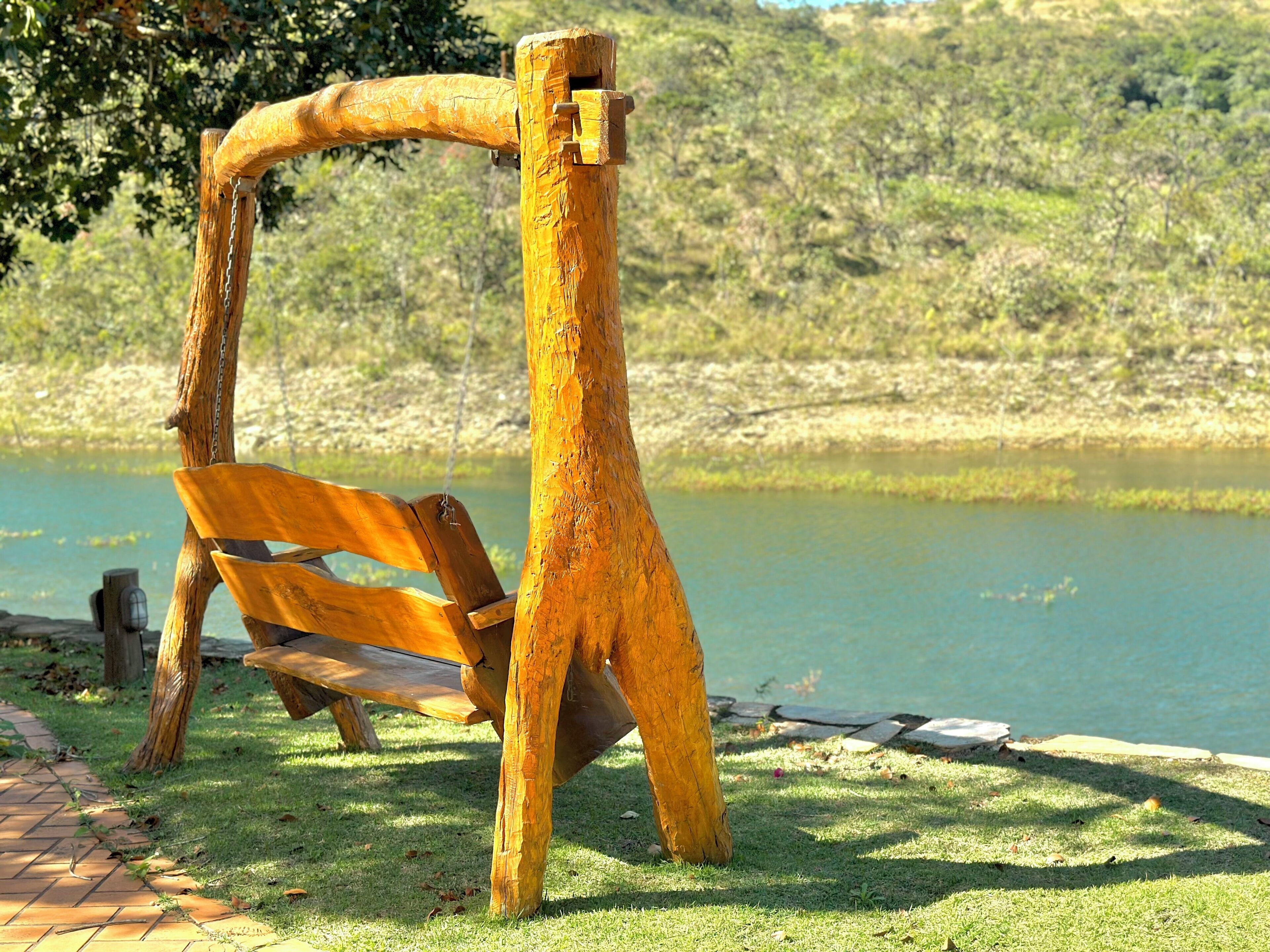 A wooden swing set by a body of water with a grassy area and a brick path.
