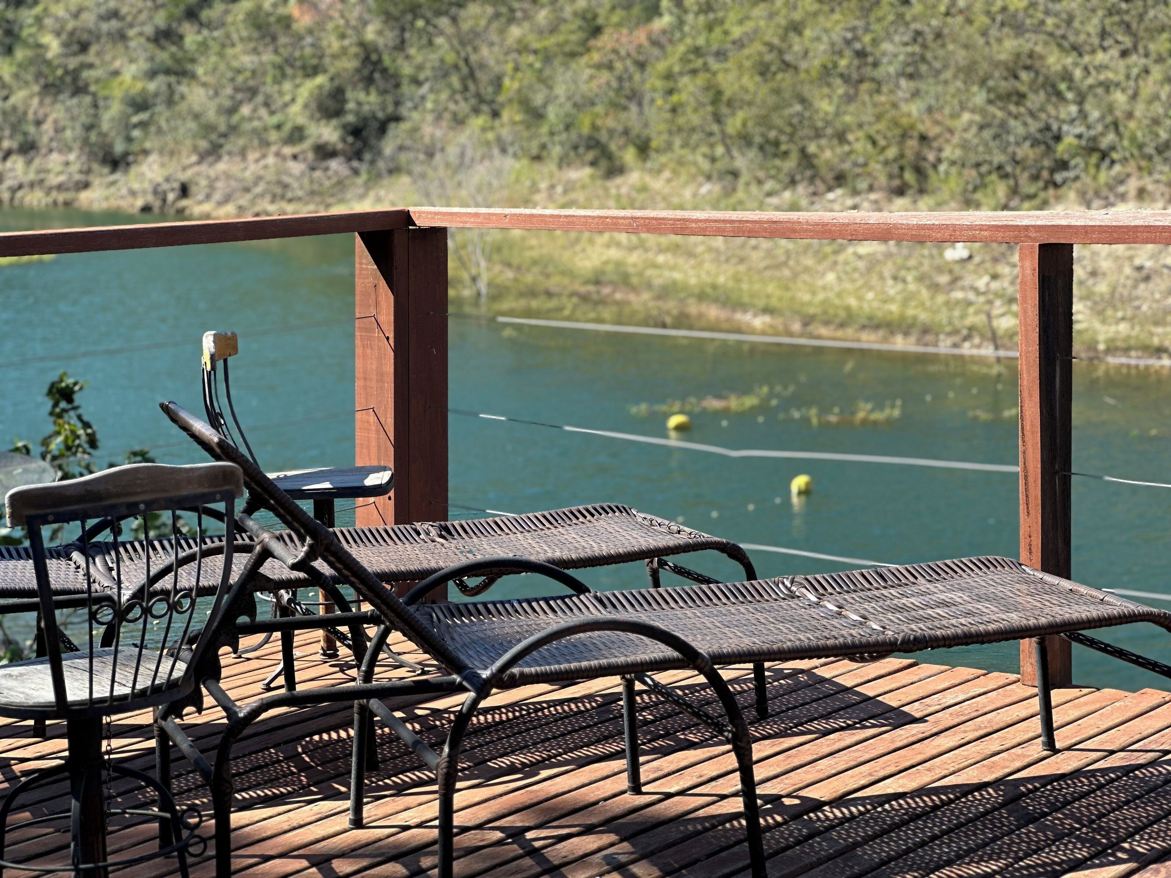 Una terraza de madera con sillas y mesas de metal con vistas a un lago.