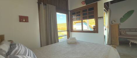 A bedroom with a large bed, a window with curtains, a wooden ceiling, and a view of the outside.
