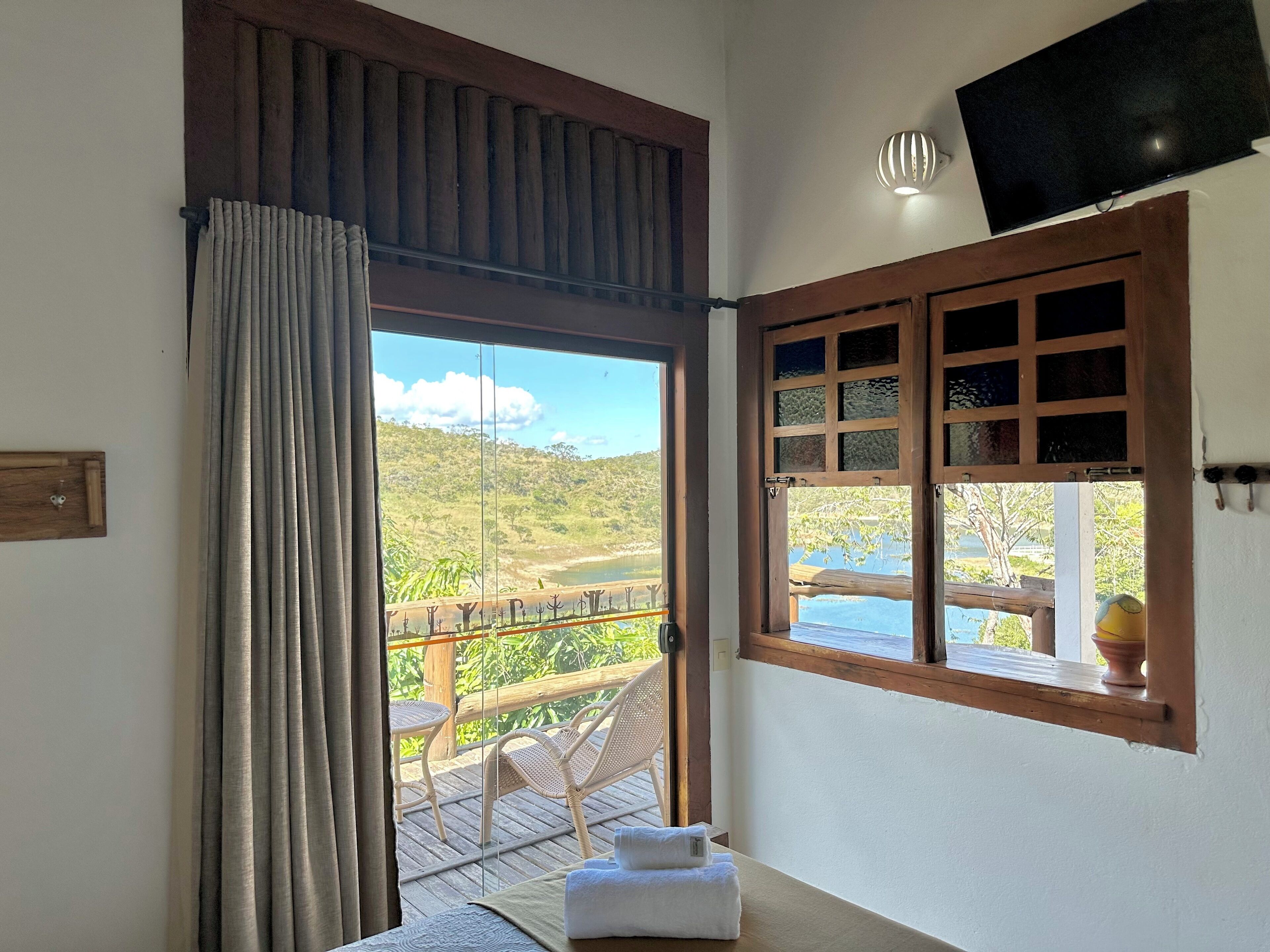 A room with a large window offering a view of a lush landscape and a wooden deck outside.