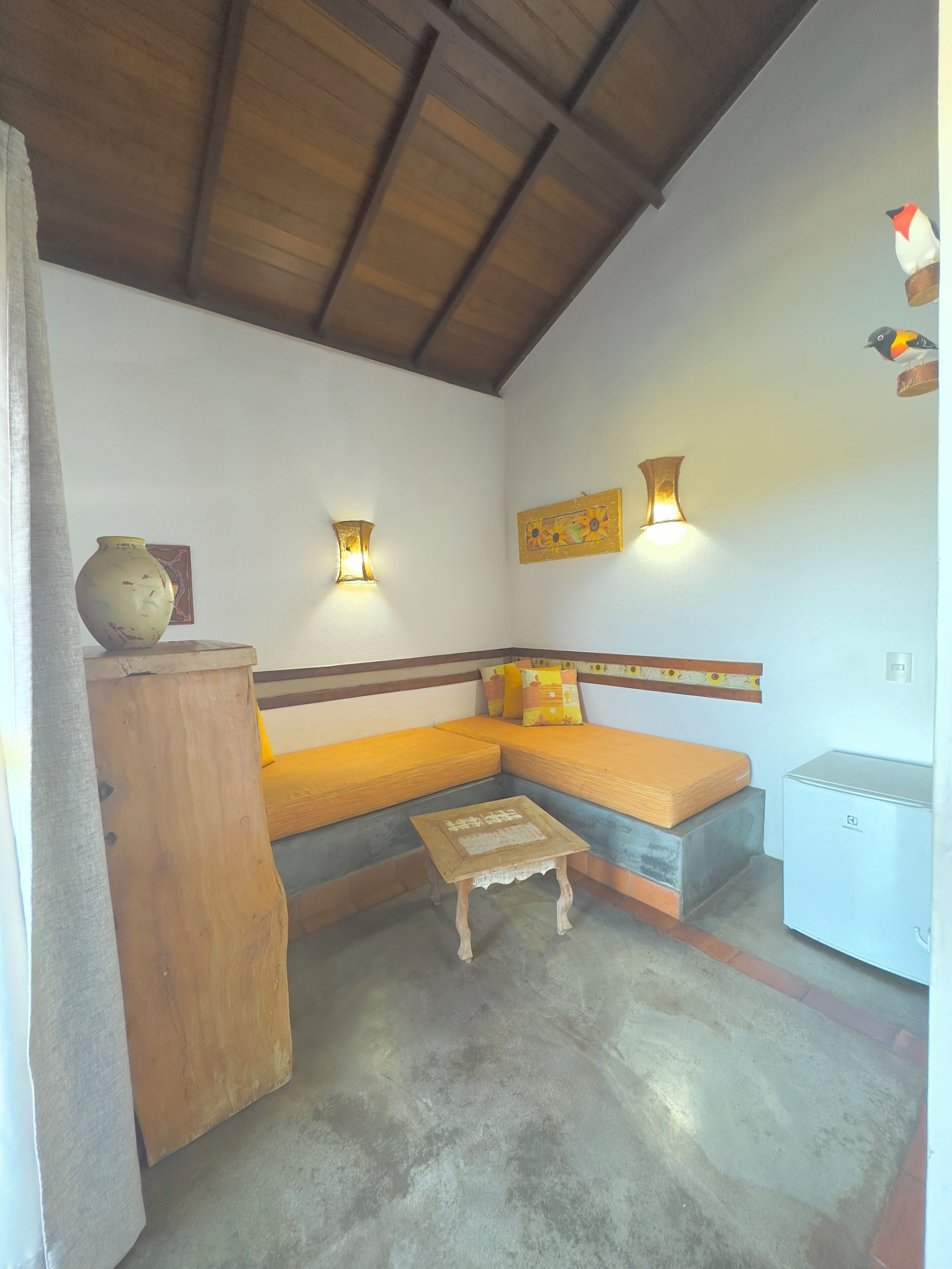 A cozy room with a wooden bench, a small table, and a refrigerator.