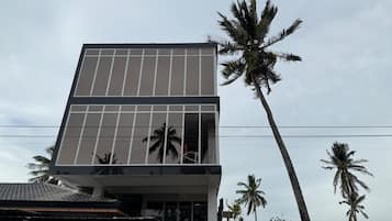 Un edificio moderno con una amplia fachada de vidrio, palmeras y una estructura de techo tradicional.