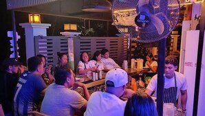 A restaurant with a neon sign, indoor seating, and a fan.