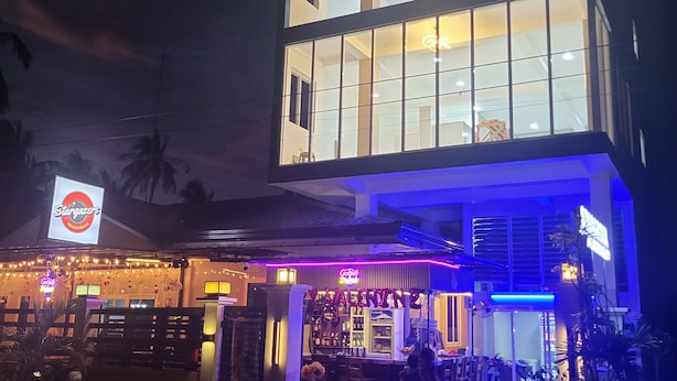 A two-story building with a bar area on the ground floor, featuring a neon sign and outdoor seating.