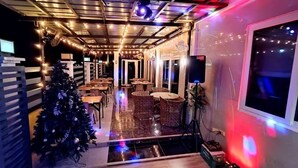 A restaurant with a Christmas tree, tables, wicker chairs, and string lights.