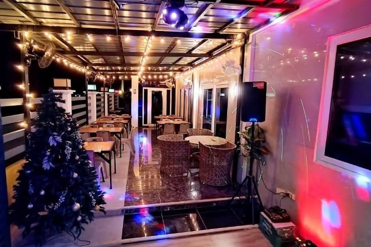 A restaurant with a Christmas tree, tables, wicker chairs, and string lights.
