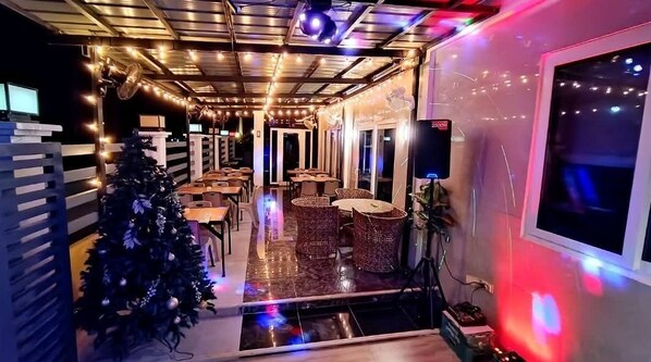 A restaurant with a Christmas tree, tables, wicker chairs, and string lights.