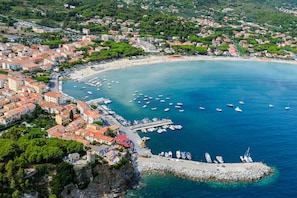 An aerial view of a coastal town with a marina, buildings with red-tiled roofs, and a clear blue sea. - Bilocale Lia a Campo (Campo nell'Elba)