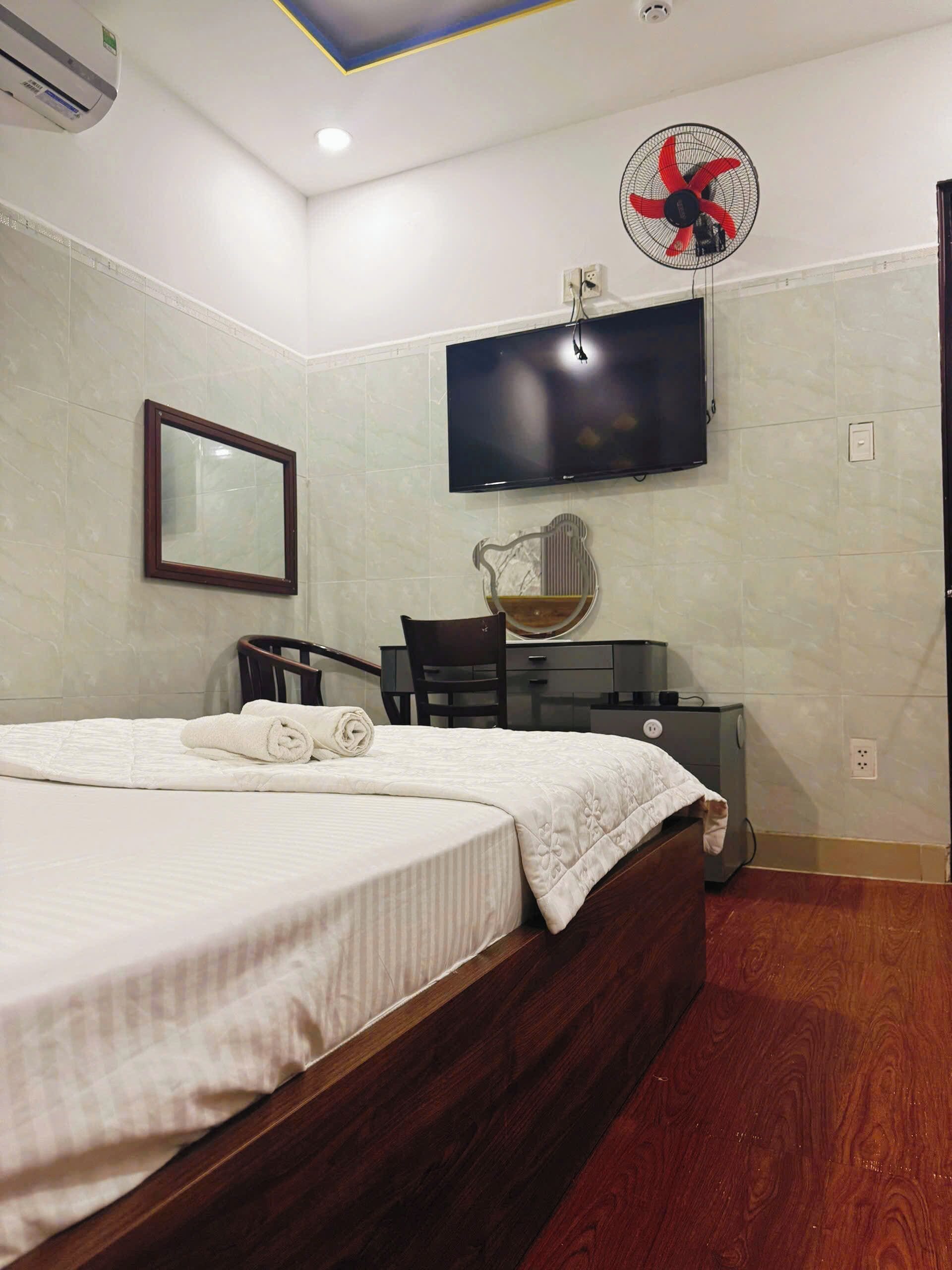 Una habitación de hotel con una cama, un escritorio, una silla, un televisor y un ventilador rojo.