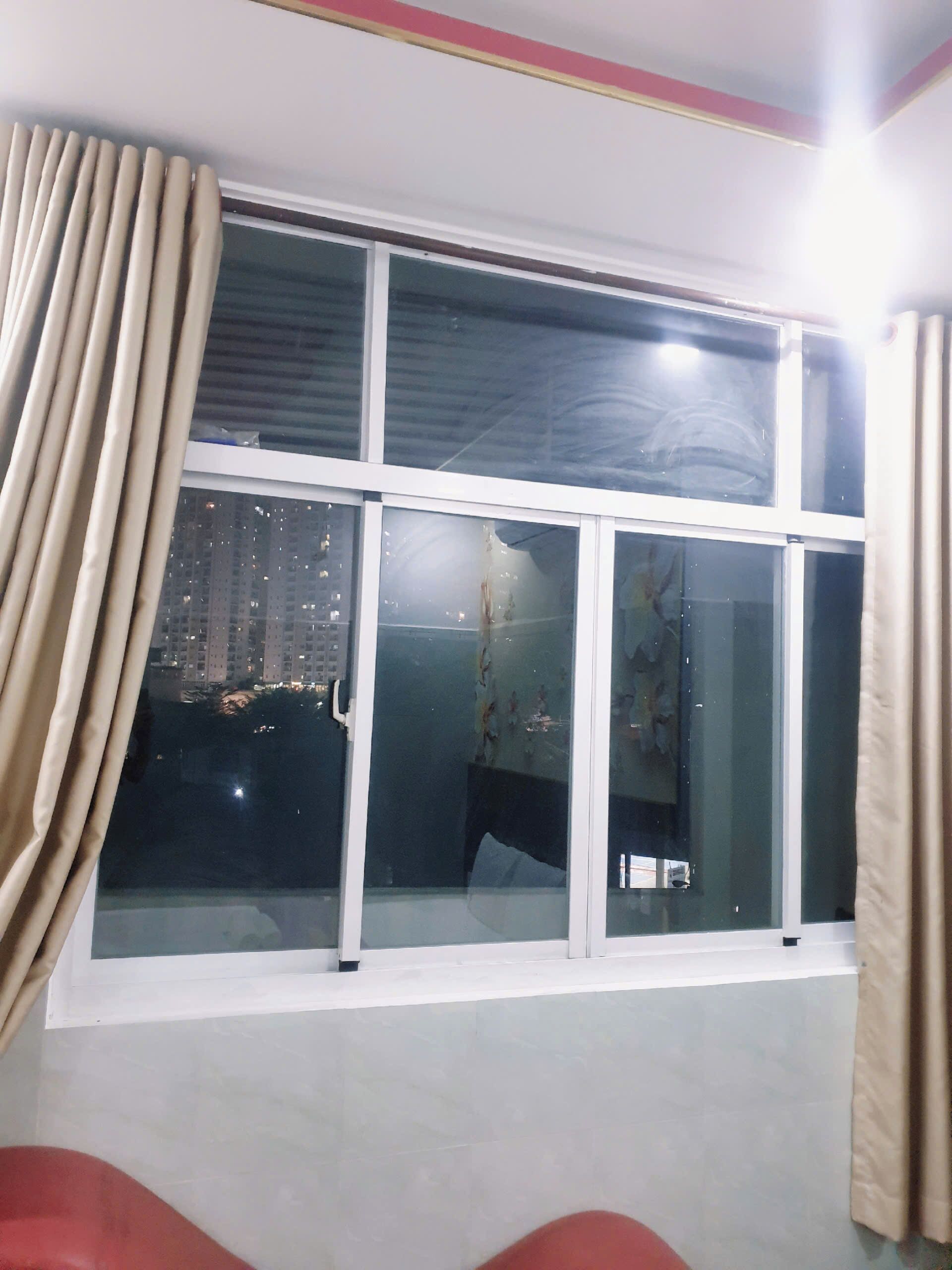 A room with a large window, curtains, and a view of a cityscape at night.