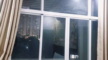 A room with a large window, curtains, and a view of a cityscape at night.