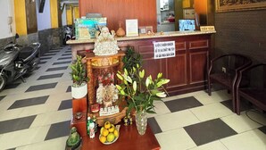 Una recepción con un cartel que dice "Double in Love Hotel" y un altar decorativo con estatuas religiosas y ofrendas.