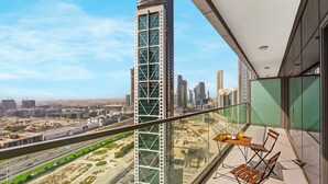 A high-rise building with a modern glass facade, a balcony with a table and chairs, and a view of a cityscape with roads and greenery. - Spectacular Burj View from Infinity Pool (Dubai)