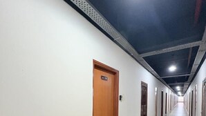 A long, narrow hallway with doors on one side and a tiled floor. - Trovero Suites (Greater Noida)