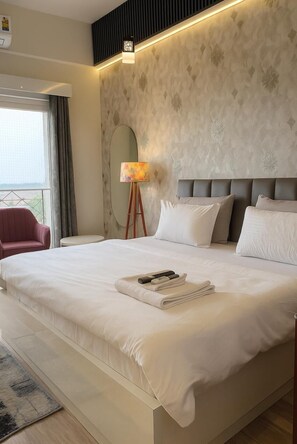 A modern hotel room with a large bed, a bedside lamp, and a view of the outdoors. - Trovero Suites (Greater Noida)
