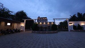 Une cour pavée avec une fontaine en pierre, un bâtiment aux fenêtres illuminées et des motos garées.