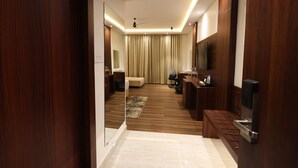 Une chambre d’hôtel avec un plancher en bois, un canapé, un bureau avec une chaise, une télévision et un minibar.
