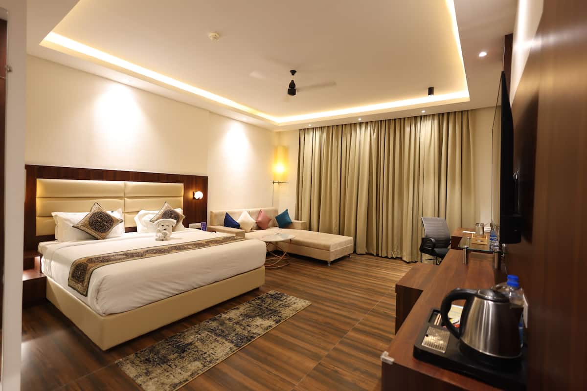 Quarto de hotel com uma cama grande, uma escrivaninha, uma cadeira, uma televisão e um ventilador de teto.