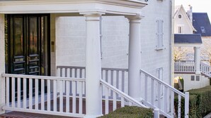 A white building with a covered porch, a brick entrance, and a white railing. - Le Parc de La Jacotte by Interhome (Deauville-Trouville)