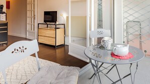 A modern living room with a wooden cabinet, a TV, a white chair, a round table with a teapot, and a glass door leading to a balcony. - Le Parc de La Jacotte by Interhome (Deauville-Trouville)