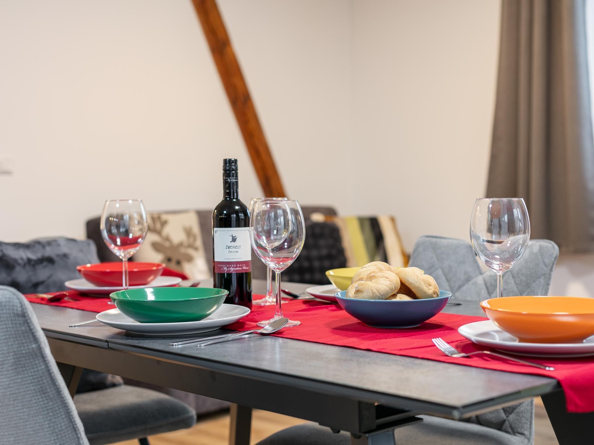 A dining table set with wine glasses, bowls, and a bottle of wine.