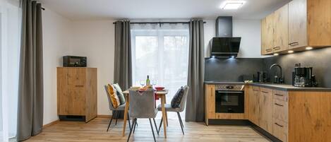 Moderni keittiö, jossa on puiset kaapit, ruokapöytä tuoleineen ja sisäänrakennettu uuni.