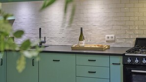 A kitchen with teal cabinets, a white brick backsplash, a gas stove, and a wine bottle on the counter. - Holiday home in Liereman nature reserve (Oud-Turnhout)