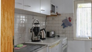 Een kleine keuken met witte kastjes, een koffiezetapparaat, een broodrooster en een fornuis.