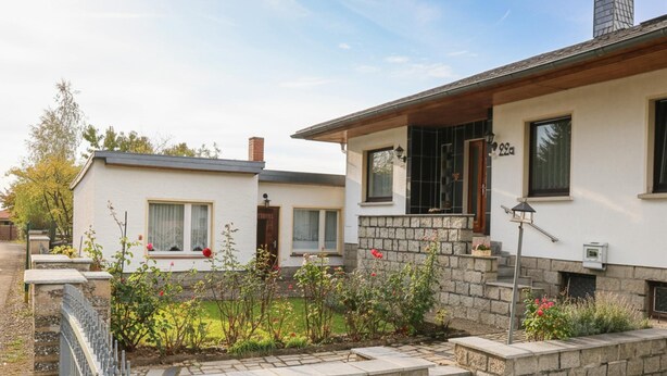Een tweelaags huis met een stenen gevel, een veranda en een kleine tuin met bloemen.