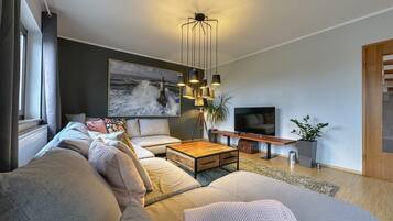 Un salon moderne avec un grand canapé, une table basse, un téléviseur et un tableau représentant un phare.