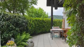 Un espace patio aménagé avec une table et des chaises, entouré d’une végétation luxuriante et offrant une vue sur un bâtiment.