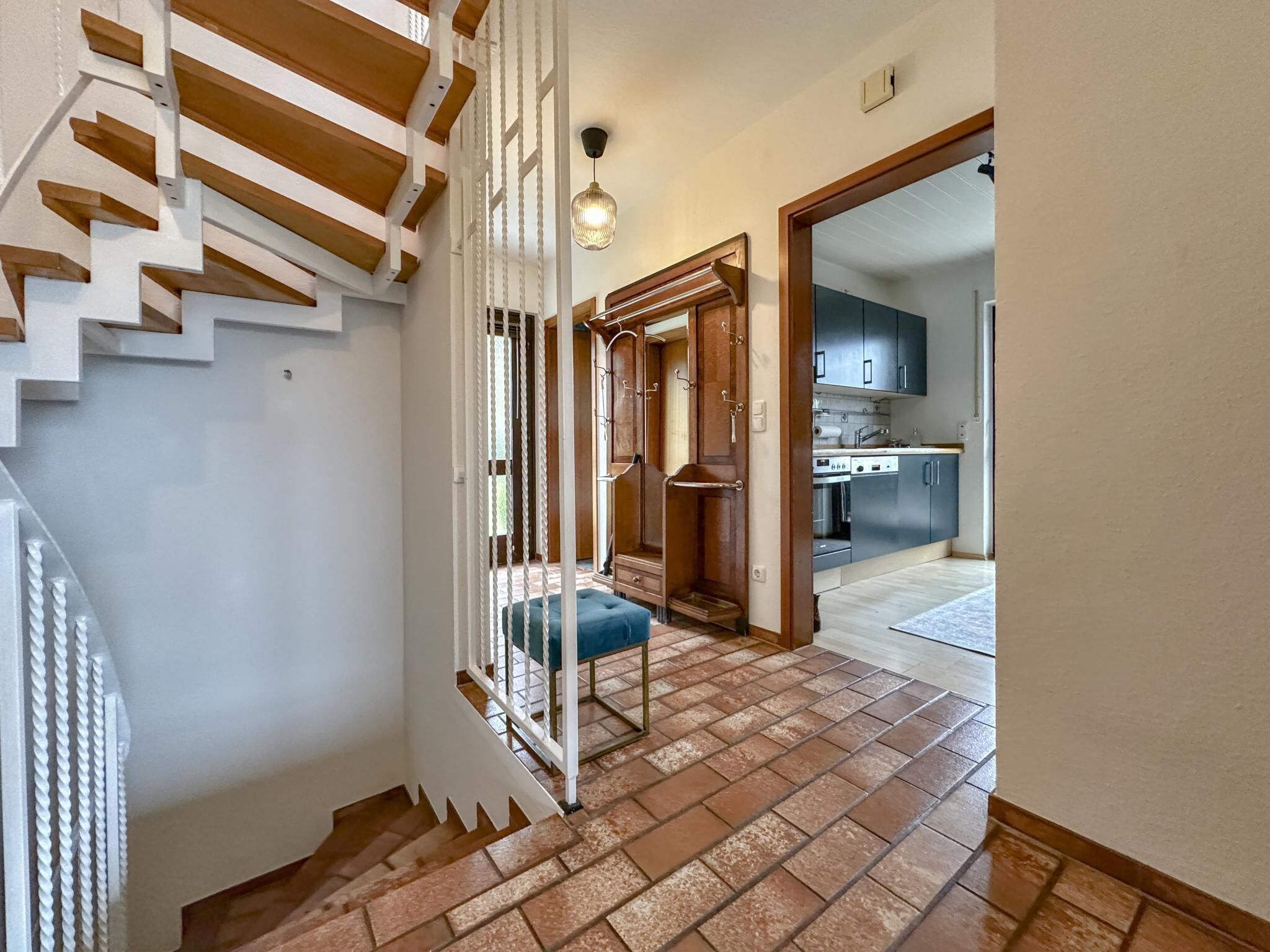 A staircase with white railings and a blue bench, leading to a kitchen area with dark cabinets and a tiled floor.