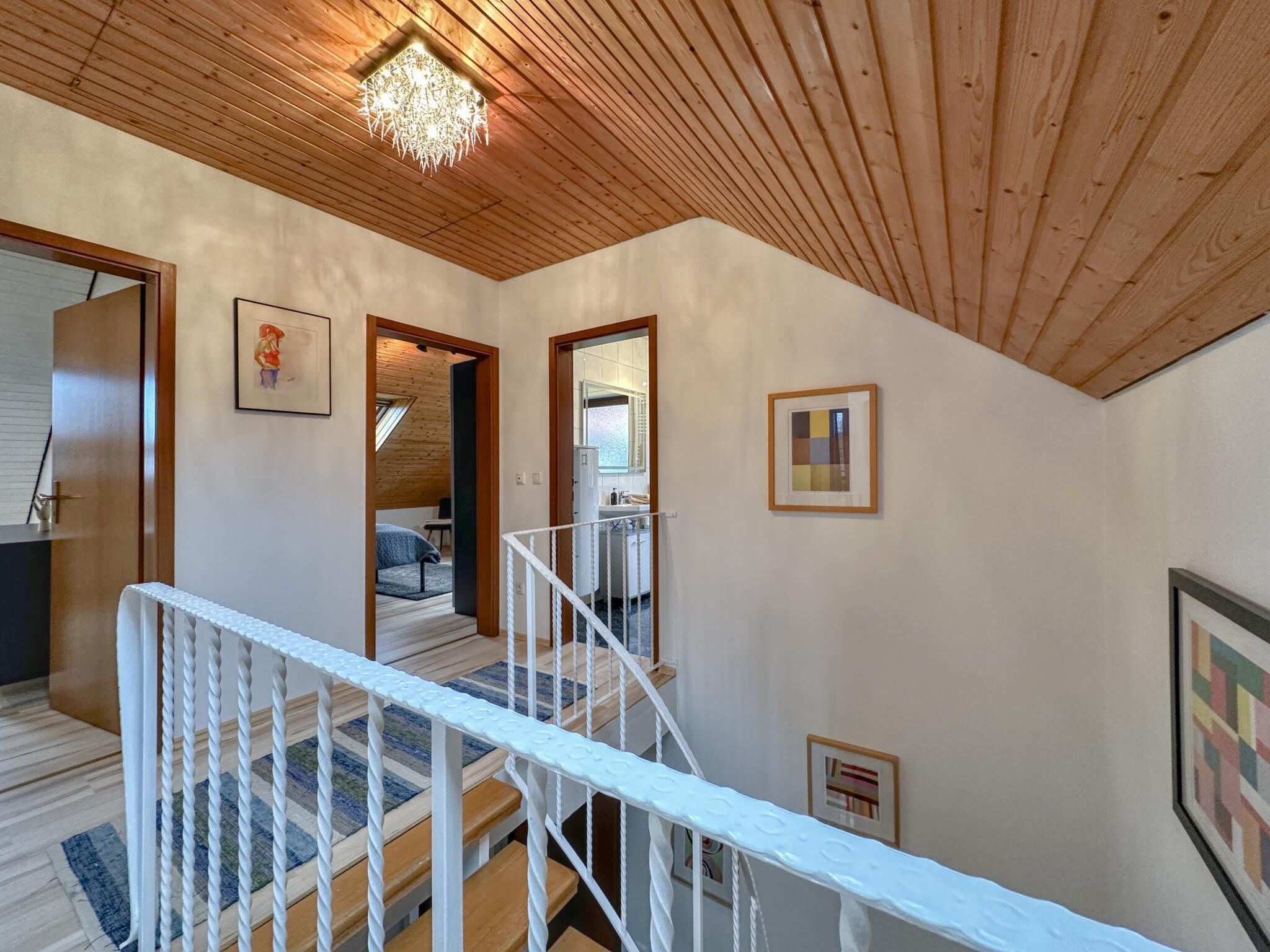 Un plafond en bois, un escalier avec des rampes blanches et un couloir orné de tableaux encadrés.