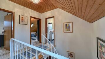 Un plafond en bois, un escalier avec des rampes blanches et un couloir orné de tableaux encadrés.