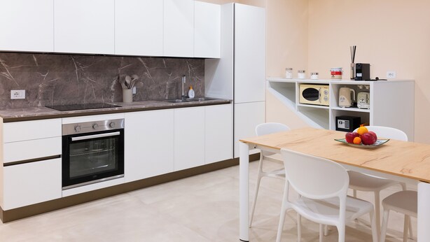 Eine moderne Küche mit weißen Schränken, einer Marmor-Spritzschutzleiste, einem eingebauten Ofen und einem Essbereich mit Holztisch und weißen Stühlen.