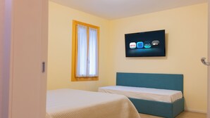 Ein Zimmer mit zwei Betten, einem Fernseher an der Wand und einem Fenster mit Vorhängen.