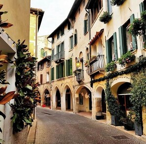 Une rue étroite bordée d’immeubles aux portes cintrées et aux balcons ornés de plantes.