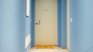 Ein schmaler Flur mit blauen Wänden, einer beigen Tür und einer gelben Fußmatte mit Text.