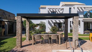 Patio esterno moderno con piscina, pilastri in pietra e una pergola.