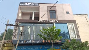 Un edificio con un letrero que indica 'Hotel Aashiyana Palace' y 'Balaji Tower' sobre un restaurante llamado 'Taste Food Delight'.