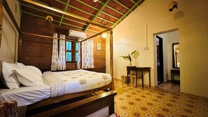 A room with a wooden bed, a small table with a plant, and a patterned floor.