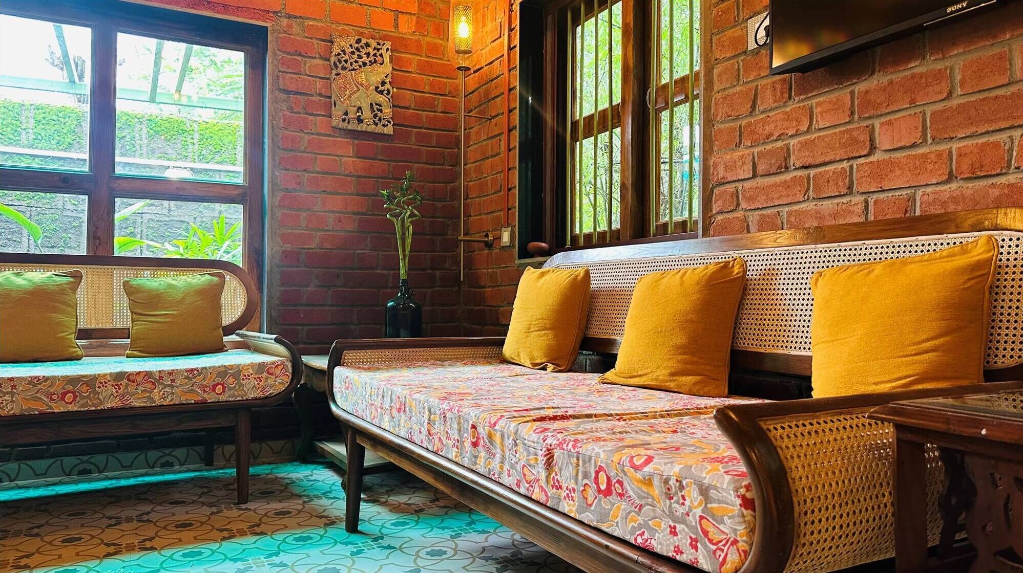 Una habitación con pared de ladrillo, un sofá con cojines amarillos, un banco acolchado y una planta en maceta.