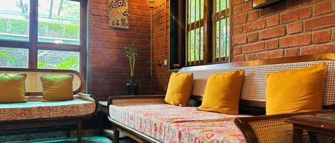 A room with a brick wall, a sofa with yellow cushions, a bench with cushions, and a potted plant.