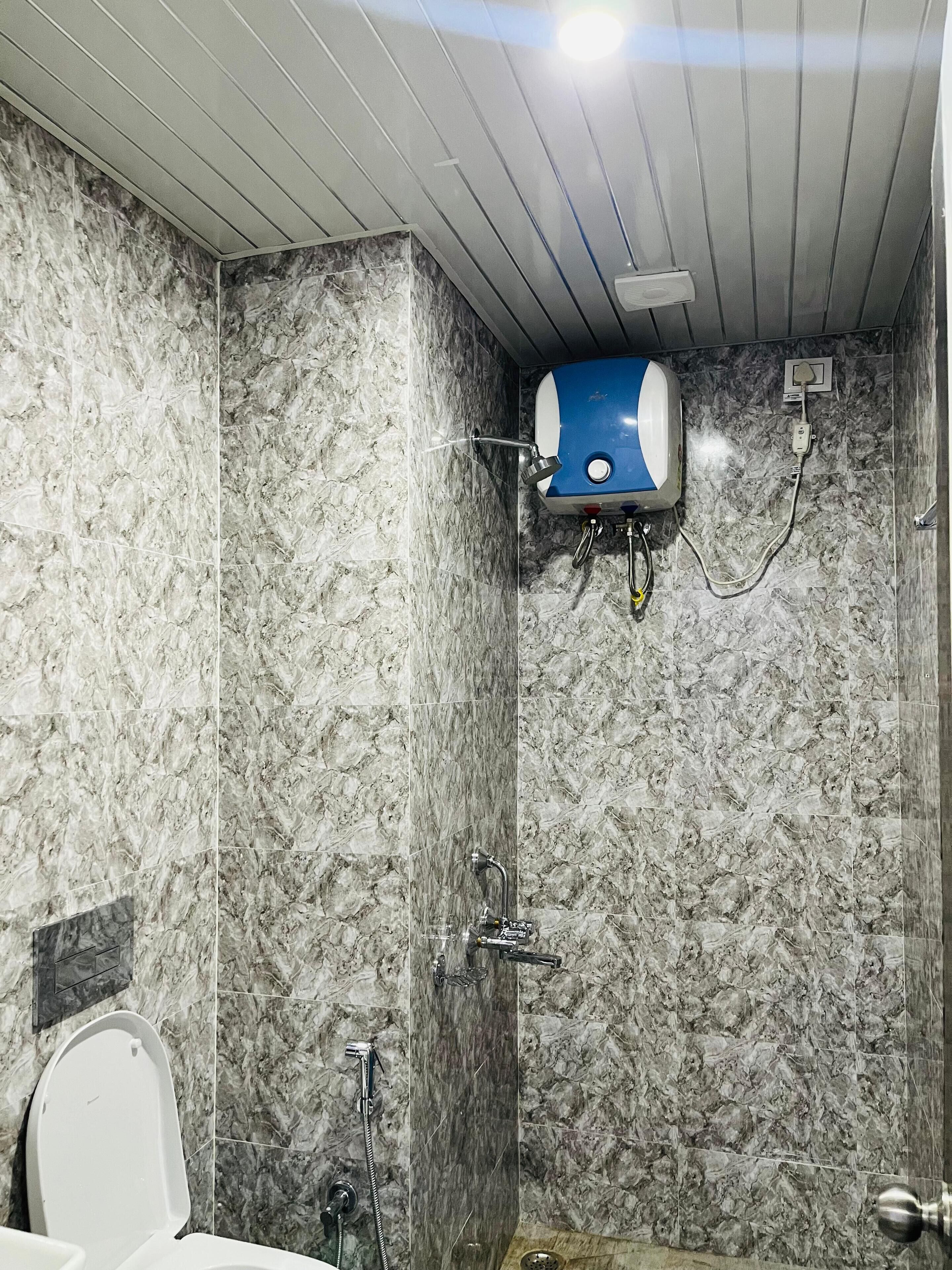 Un baño con pared de mármol, inodoro, ducha con cabezal de ducha manual y calentador de agua azul.