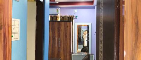 A hotel corridor with a wooden door frame, a desk with a chair, and a mirror reflecting a person.