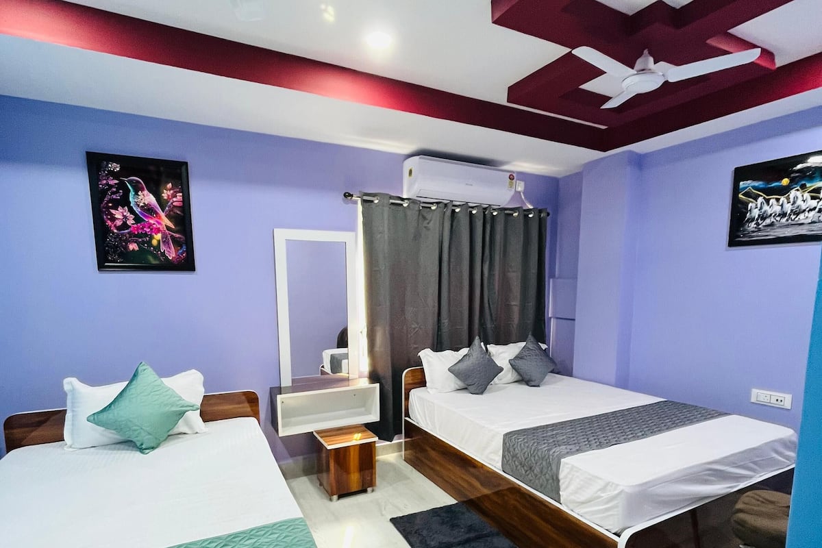 Quarto moderno com duas camas, um ventilador de teto e uma pequena mesa de cabeceira com abajur.